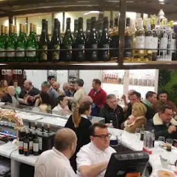 Clientes alrededor de la barra bajo una hilera de botellas de vino