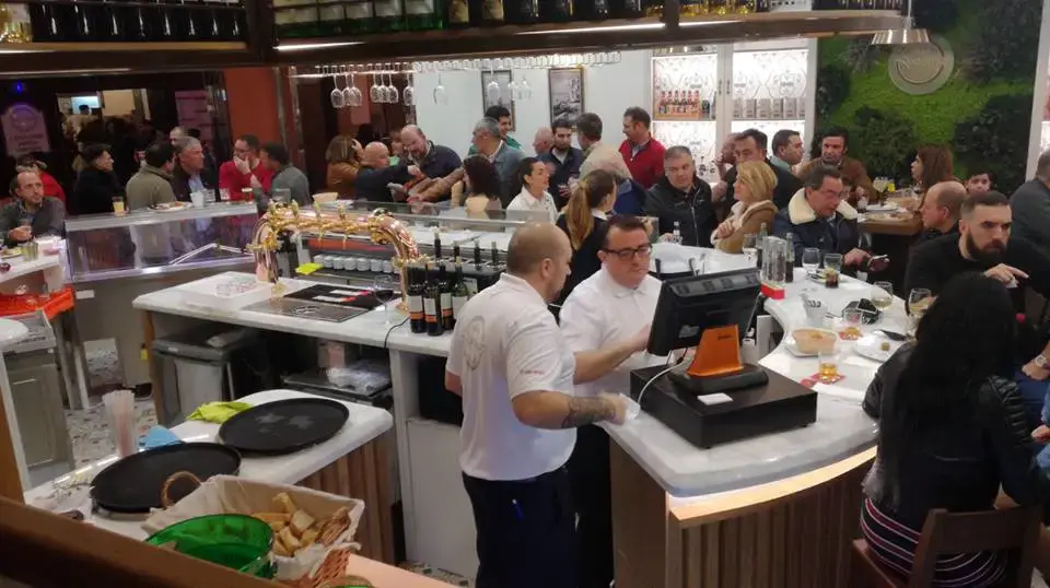 Camareros tras la barra atendiendo a un local lleno de clientes