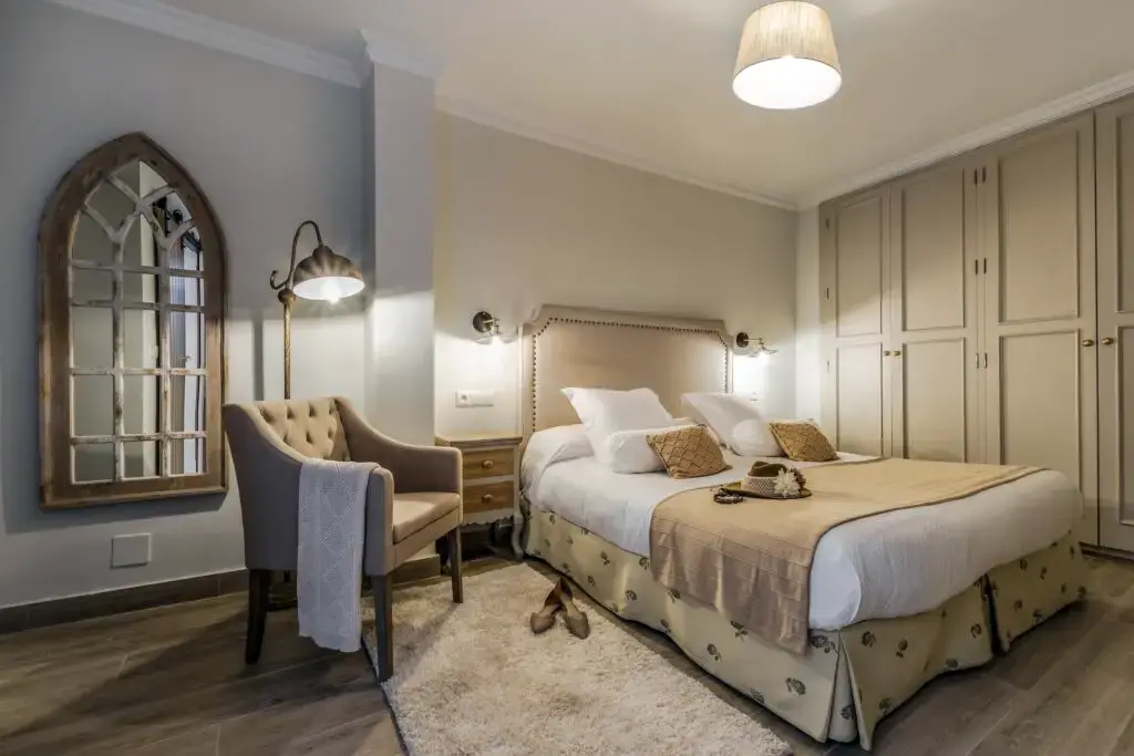Dormitorio con cama de matrimonio, butaca tapizada, espejo con forma de ventana y armario empotrado