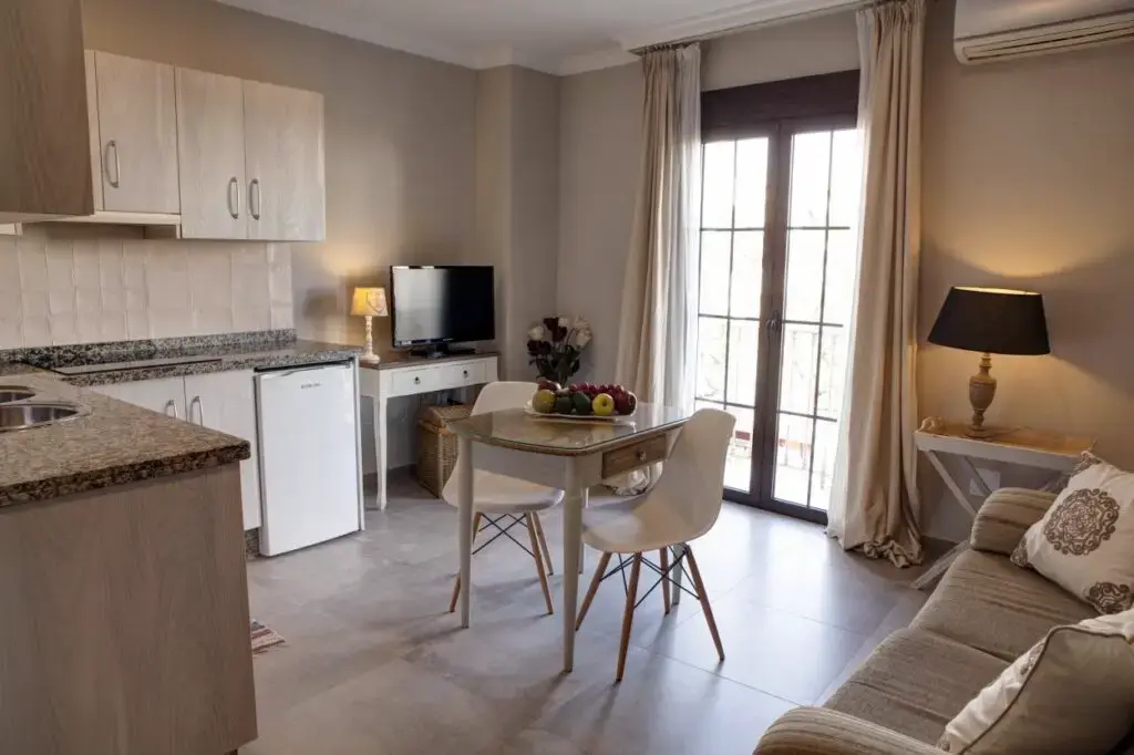 Apartamento con cocina, mesa de comedor con sillas blancas, sofá y puerta acristalada