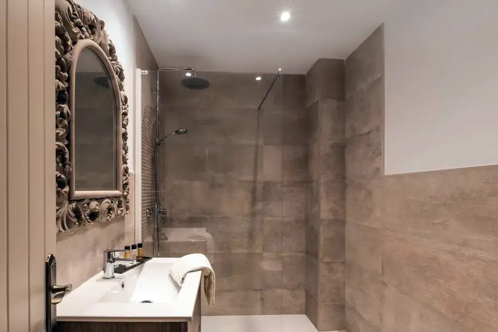 Baño con ducha de lluvia, paredes de piedra y espejo con marco tallado
