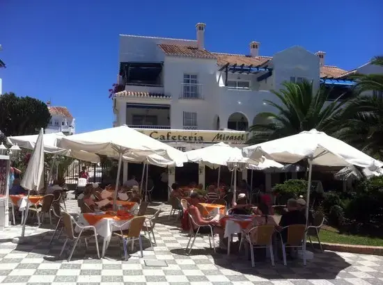 Terraza de la Cafetería Mirasol con sombrillas blancas y manteles naranjas en un día soleado