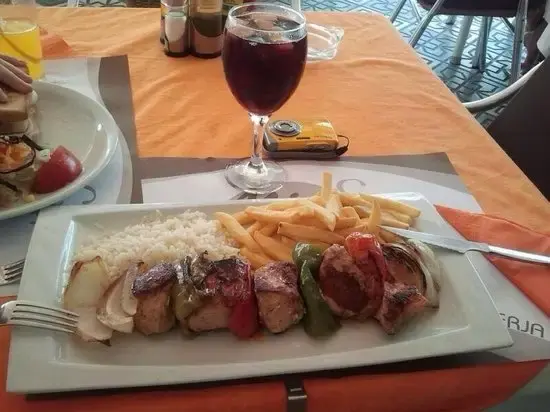 Brocheta de carne y verduras con patatas fritas y arroz, junto a una copa de sangría