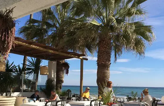 Clientes comiendo bajo un porche de cañas y palmeras, con el mar al fondo
