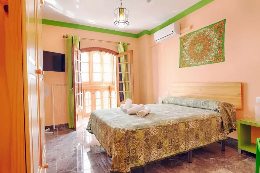 Habitación con cama de matrimonio, colcha estampada, aire acondicionado y balcón con cortinas verdes