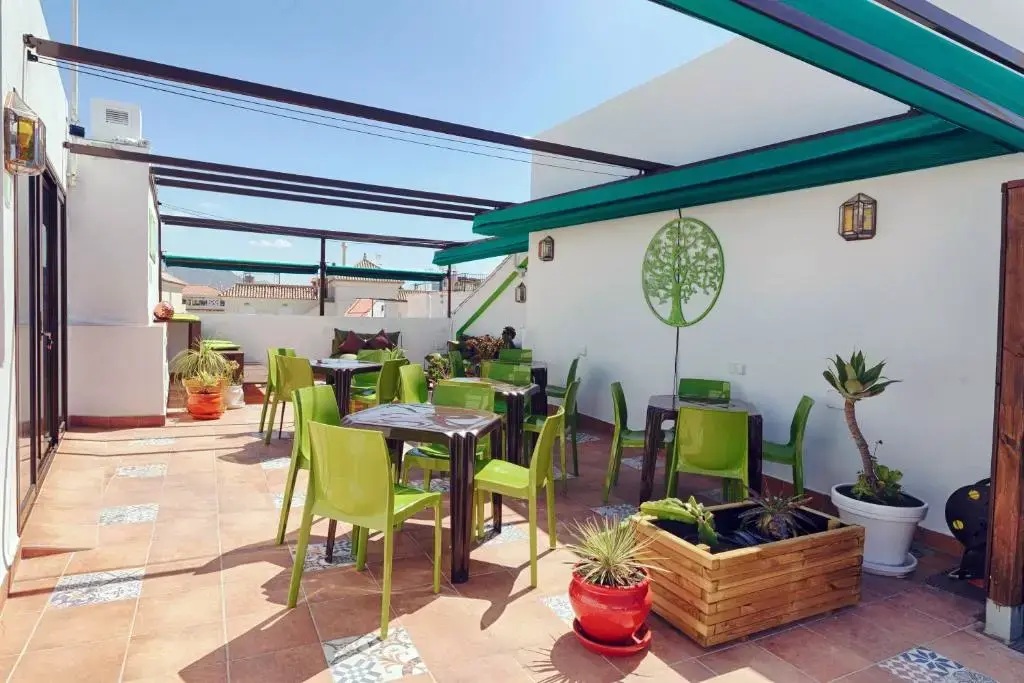 Terraza con sillas verdes, mesas, plantas en macetas y pérgola con toldos