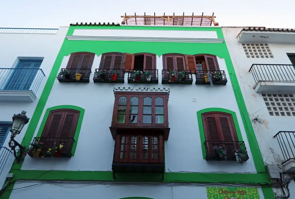 Fachada blanca y verde del Charming Nerja Hostel con mirador de madera y balcones con macetas