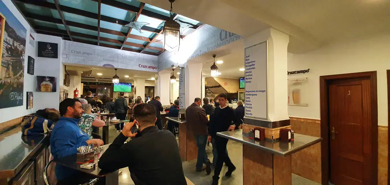 Barra y mesas altas del bar con lámparas colgantes y clientes tomando algo