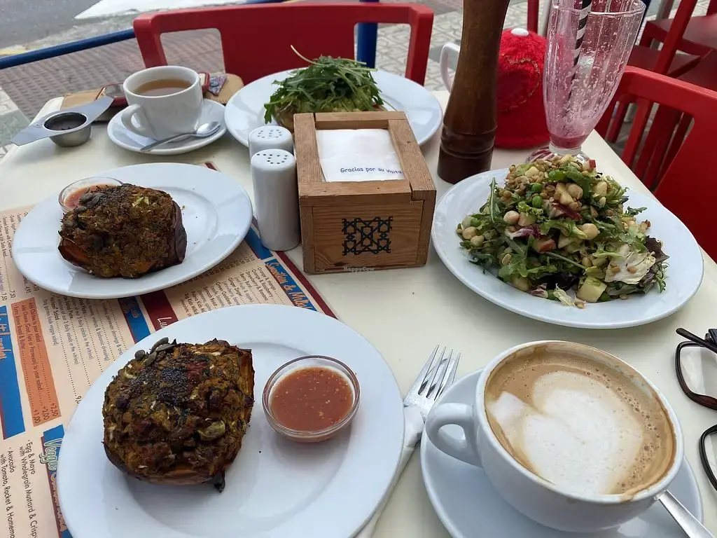 Mesa con dos bollos salados, ensalada de legumbres, rúcula y café con leche