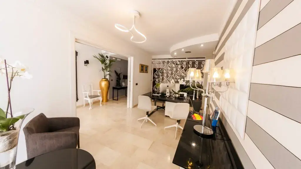 Recepción del Hostal Abril con mostrador negro, sillas blancas y pared de rayas grises