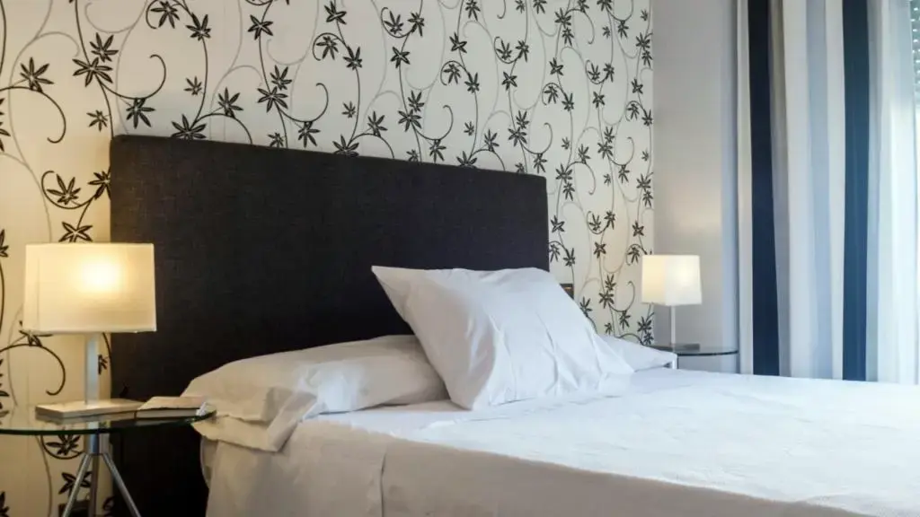Cama con cabecero negro acolchado, lámparas de mesa y papel pintado de flores