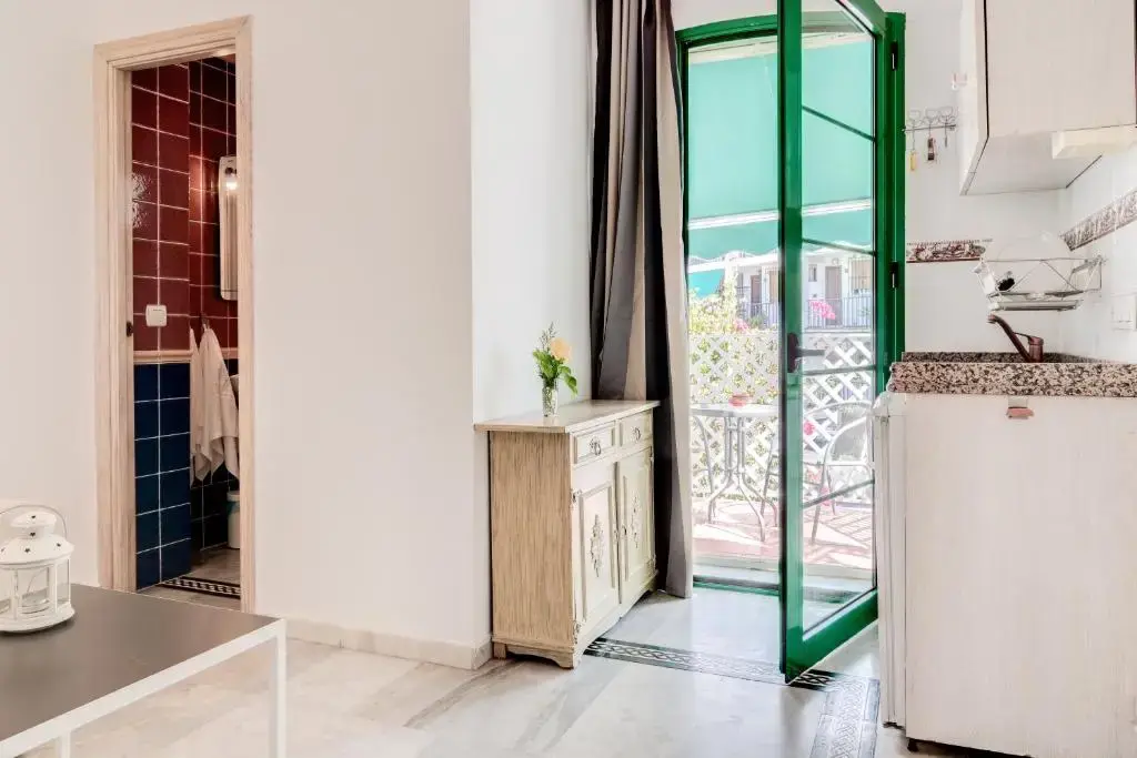 Estudio con cocina, baño de azulejos y puerta verde a un balcón con mesa