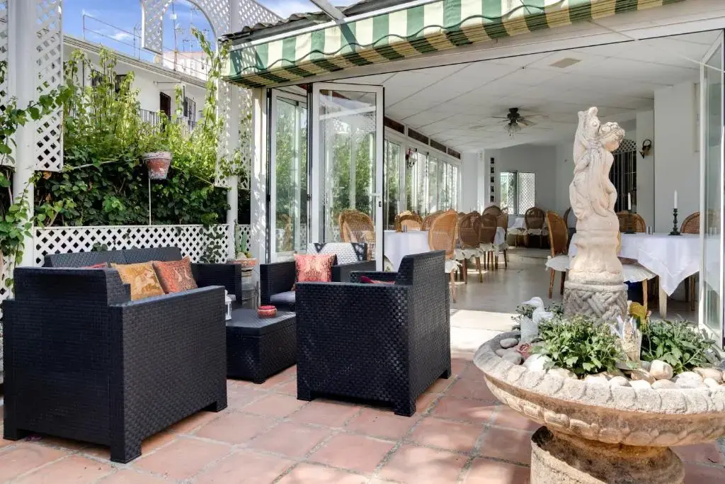 Terraza junto al comedor acristalado, con sillones de ratán y estatua sobre una fuente