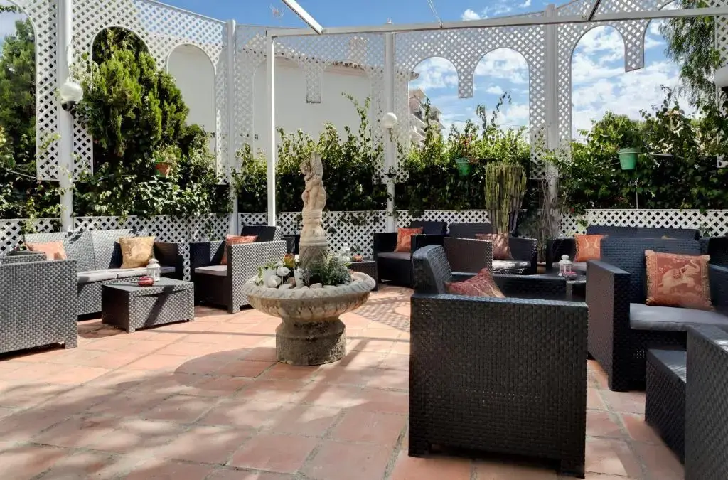 Terraza con sofás de ratán negro, celosías blancas y una fuente de piedra en el centro