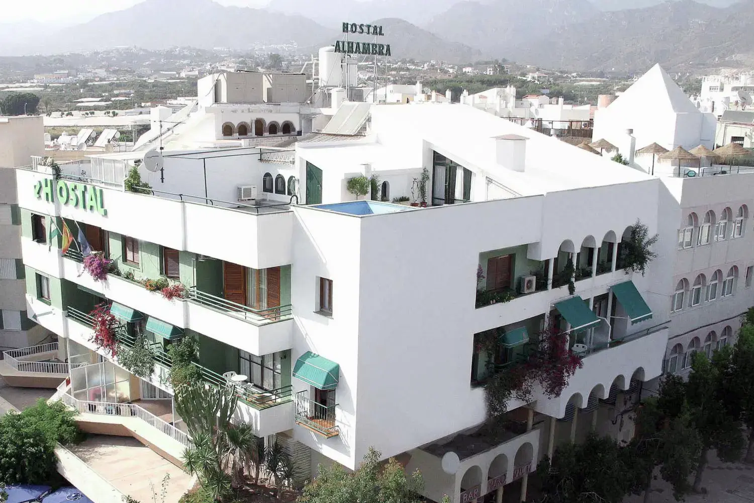 Vista aérea del Hostal Alhambra con toldos verdes, buganvillas y los montes al fondo
