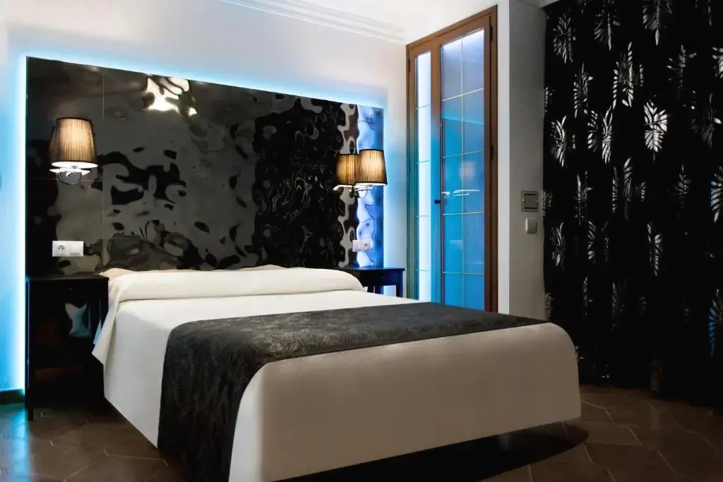 Habitación con cabecero negro brillante iluminado en azul, apliques y cortinas estampadas