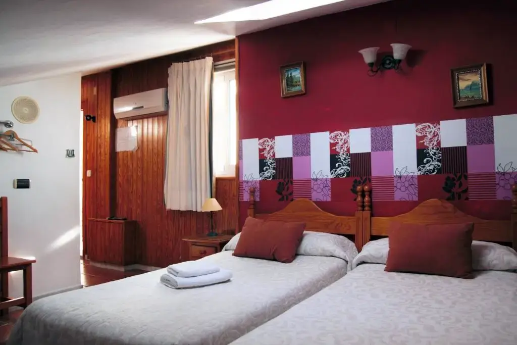 Habitación con dos camas juntas, pared granate y aire acondicionado