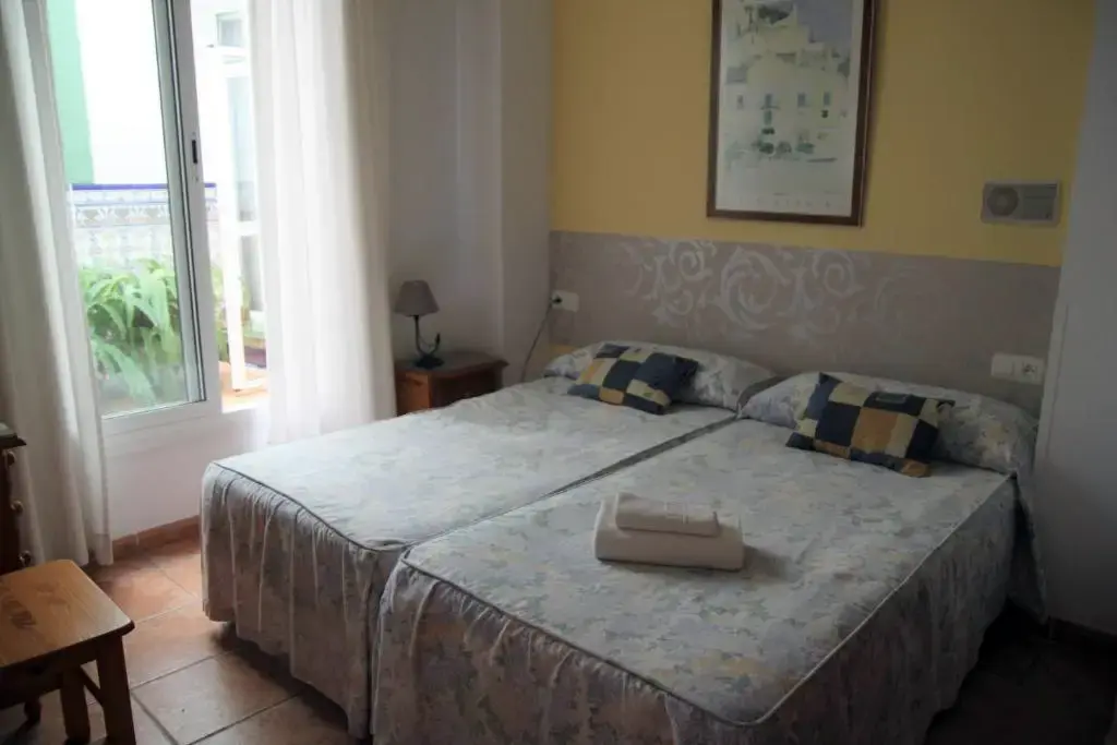 Habitación con dos camas, colchas estampadas y ventana a un patio con plantas