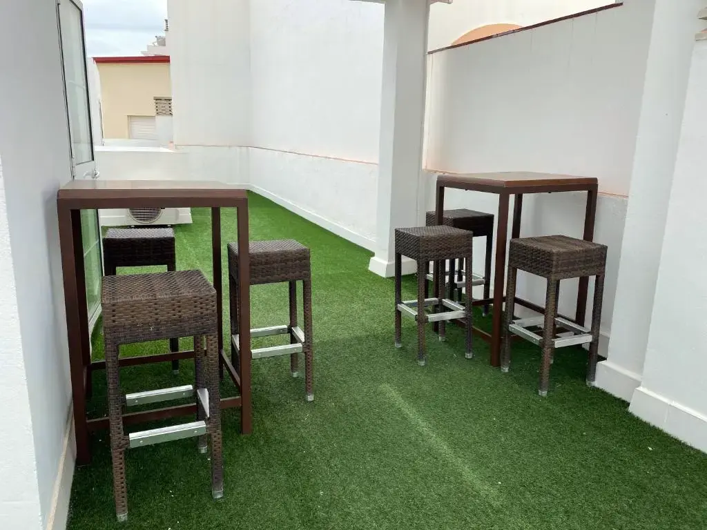 Mesas altas y taburetes de mimbre sobre césped artificial en la terraza del hostal