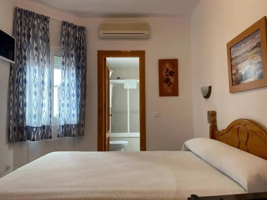 Habitación doble con cabecero de madera, cortinas estampadas y baño al fondo