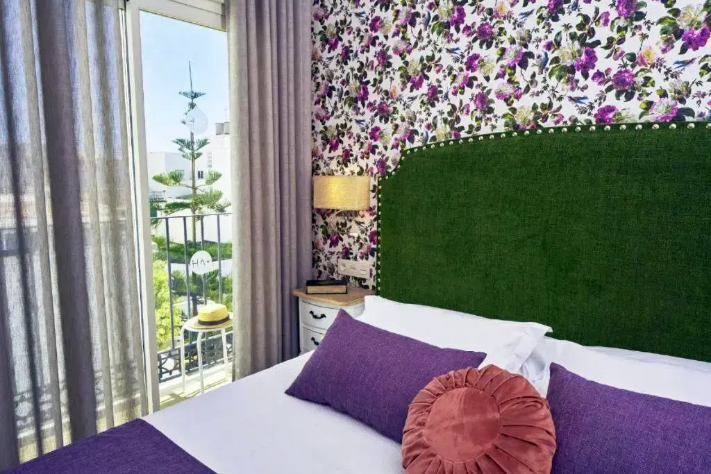 Habitación con cabecero verde, papel pintado de flores y balcón con vistas a la calle