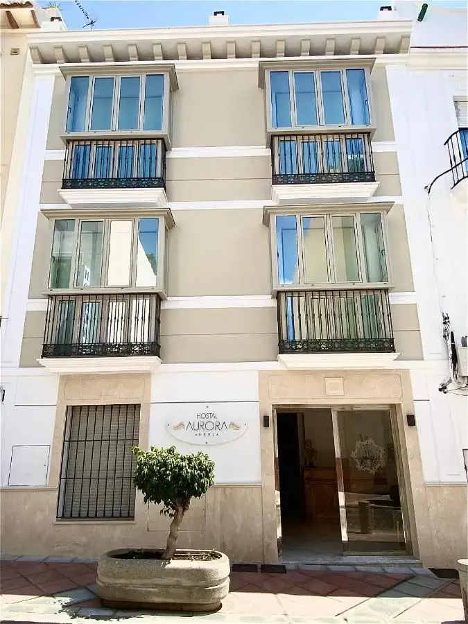 Fachada del Hostal Aurora con miradores acristalados, balcones de forja y un árbol en maceta