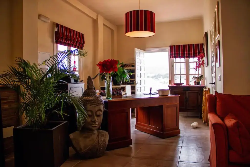Recepción con escritorio de madera, busto de Buda, palmera en maceta y sofá rojo