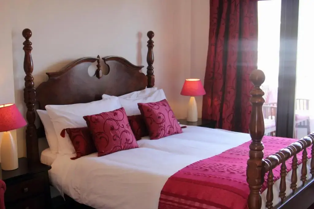 Cama de matrimonio con cabecero de madera torneada, cojines granate y lámparas rojas