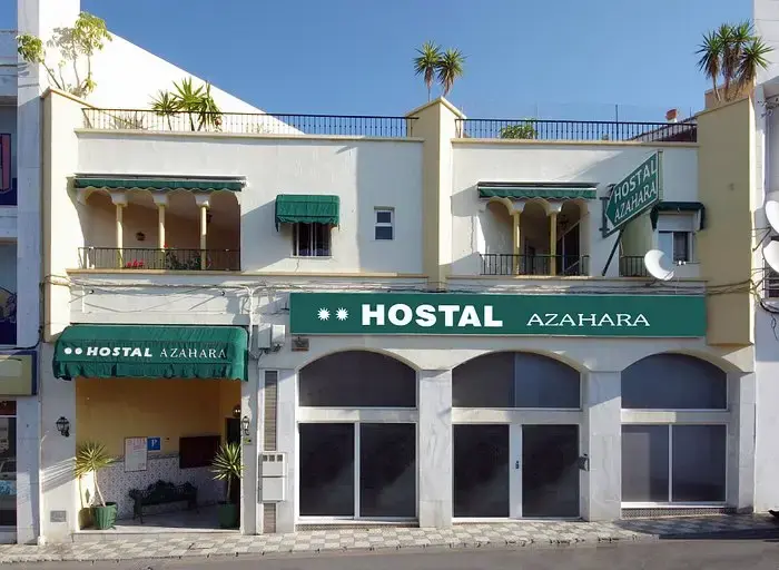 Fachada blanca del Hostal Azahara con toldos verdes y terraza en la azotea