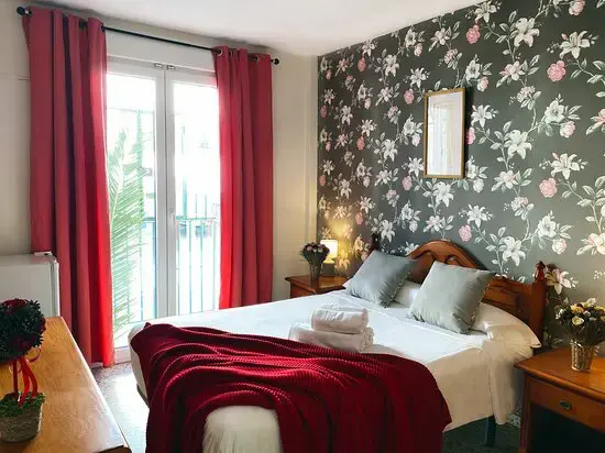 Habitación con cama de matrimonio, papel pintado de flores y cortinas rojas junto al balcón