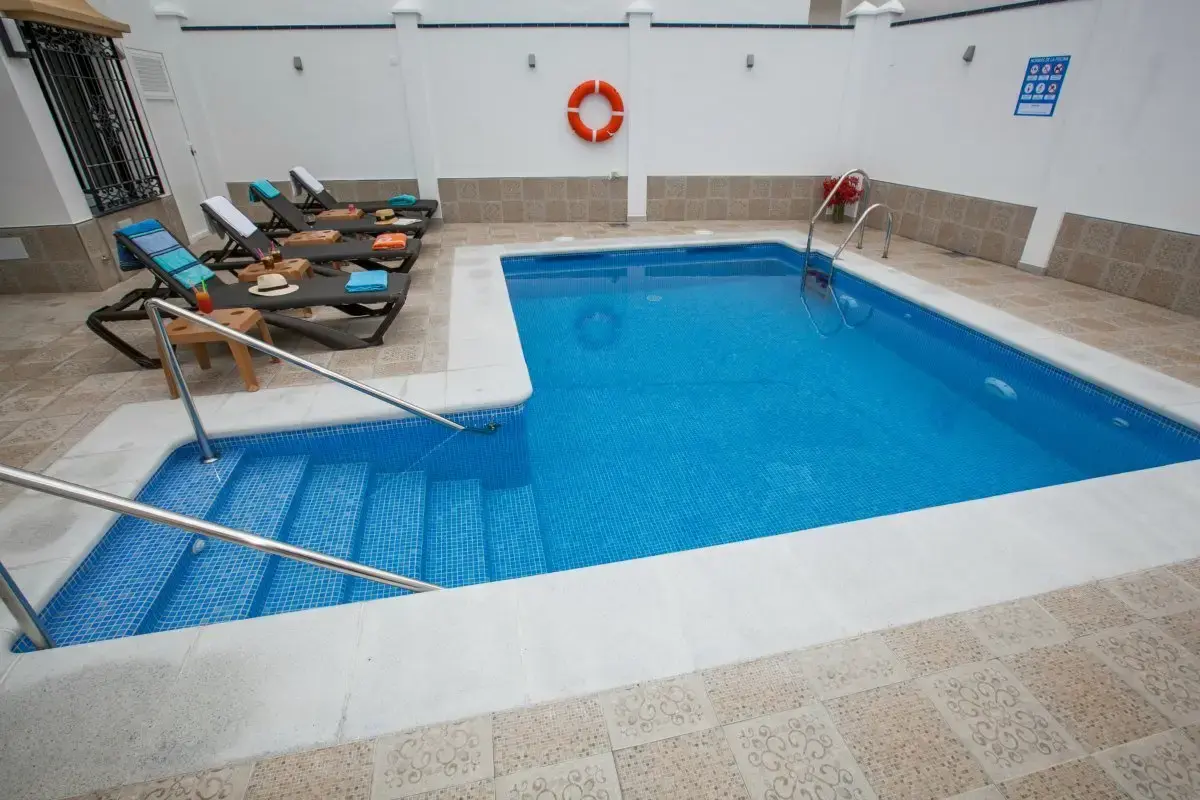Piscina con escalera de obra y tumbonas en el patio interior del Hostal Boutique Bajamar