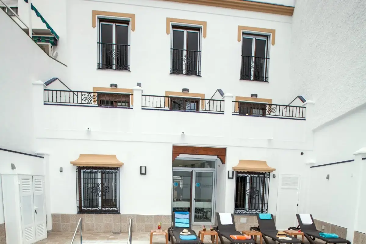 Patio de la piscina con tumbonas frente a la fachada interior blanca con rejas y balcones