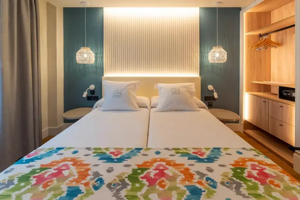 Habitación con dos camas juntas, colcha de colores, lámparas colgantes y armario abierto