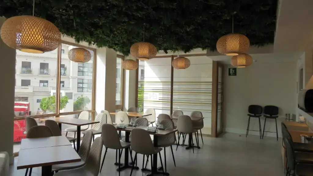 Comedor con mesas puestas, grandes ventanales a la calle y lámparas de bambú