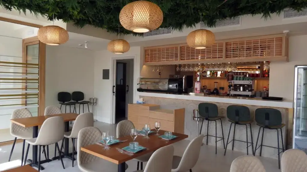 Cafetería con barra, taburetes, lámparas de mimbre y techo cubierto de vegetación
