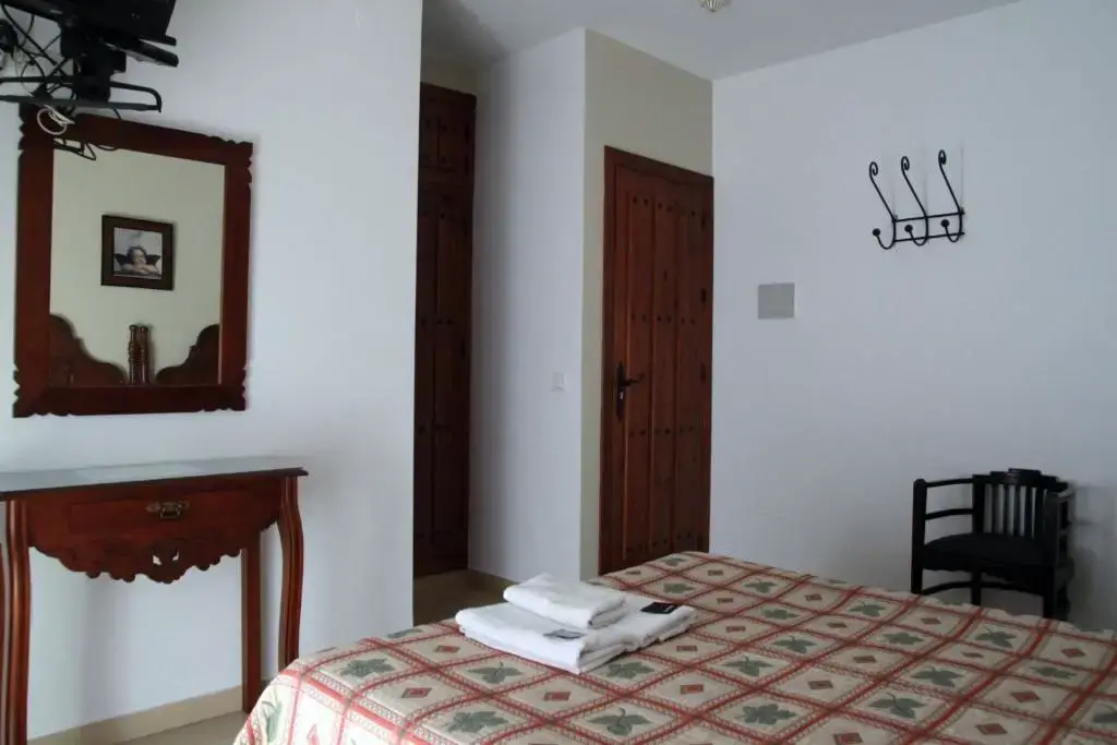 Habitación con cama de colcha estampada, consola y espejo de madera tallada y perchero