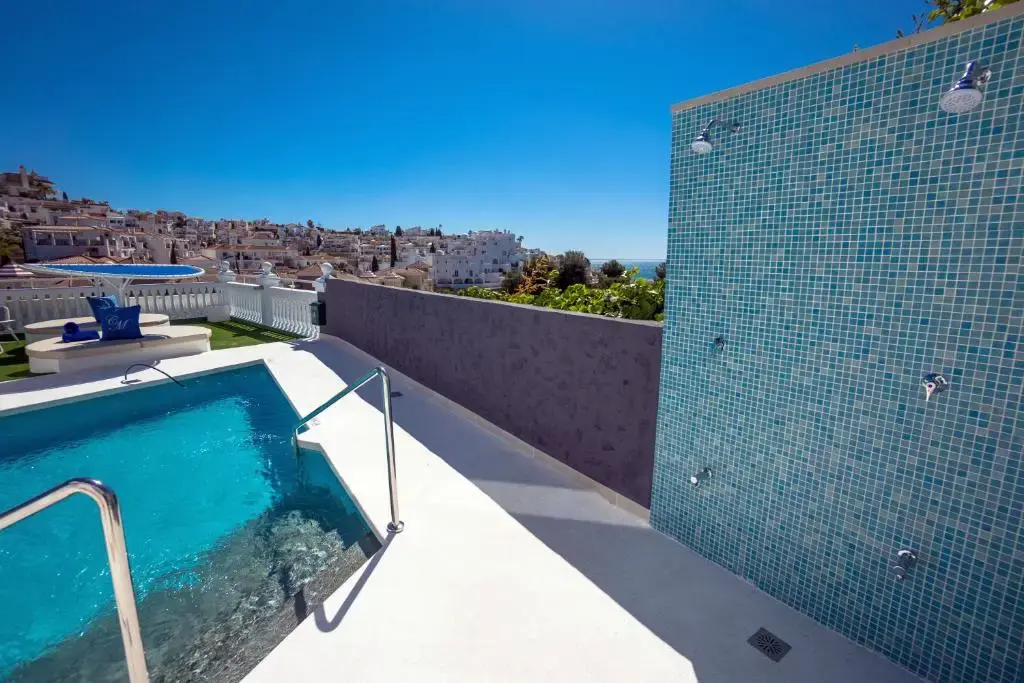 Piscina con escalerilla y pared de duchas de gresite, con casas de Nerja y el mar al fondo