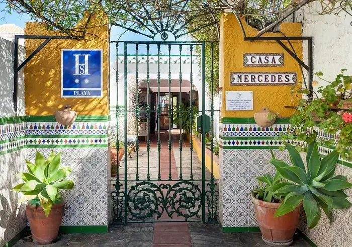 Entrada de Casa Mercedes con cancela verde de forja, azulejos, placa de hostal y macetas
