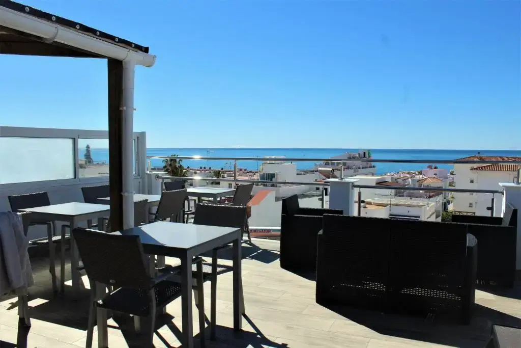 Terraza en la azotea con mesas, sofás de ratán y vistas al mar sobre los tejados