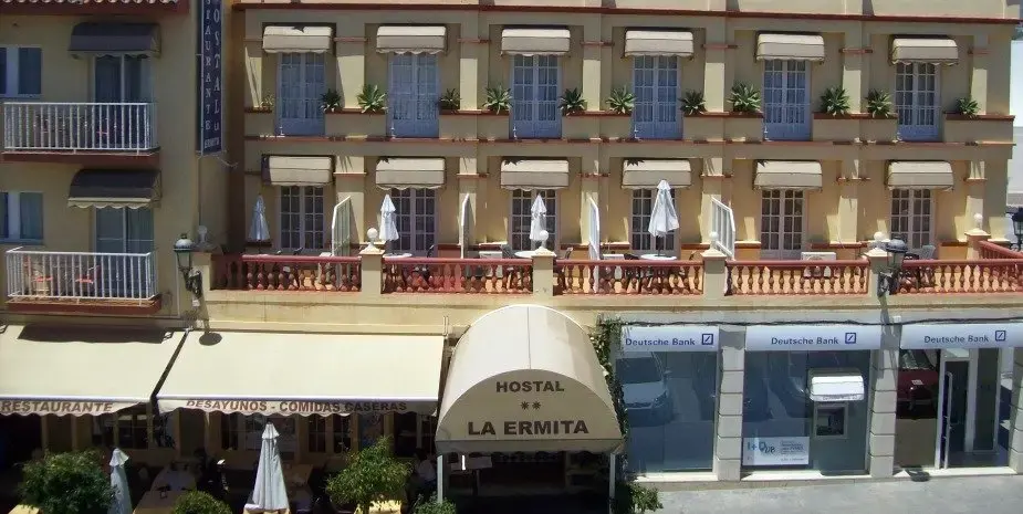 Fachada del Hostal La Ermita con toldo de entrada, balcones y terraza con sombrillas