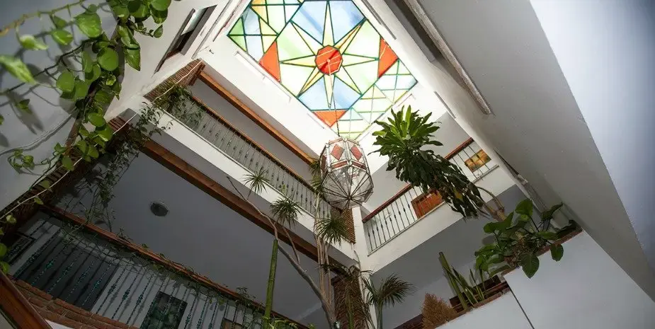 Patio interior visto desde abajo, con plantas, farol y lucernario de vidriera de colores