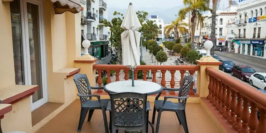 Terraza con mesa y sillas de forja sobre una calle con palmeras del centro de Nerja