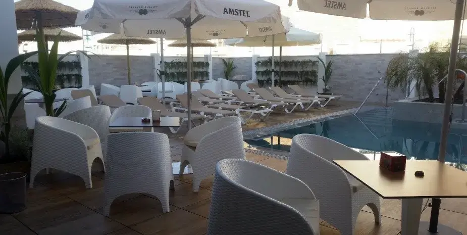 Zona de piscina con sillones blancos de mimbre, sombrillas y tumbonas junto al agua