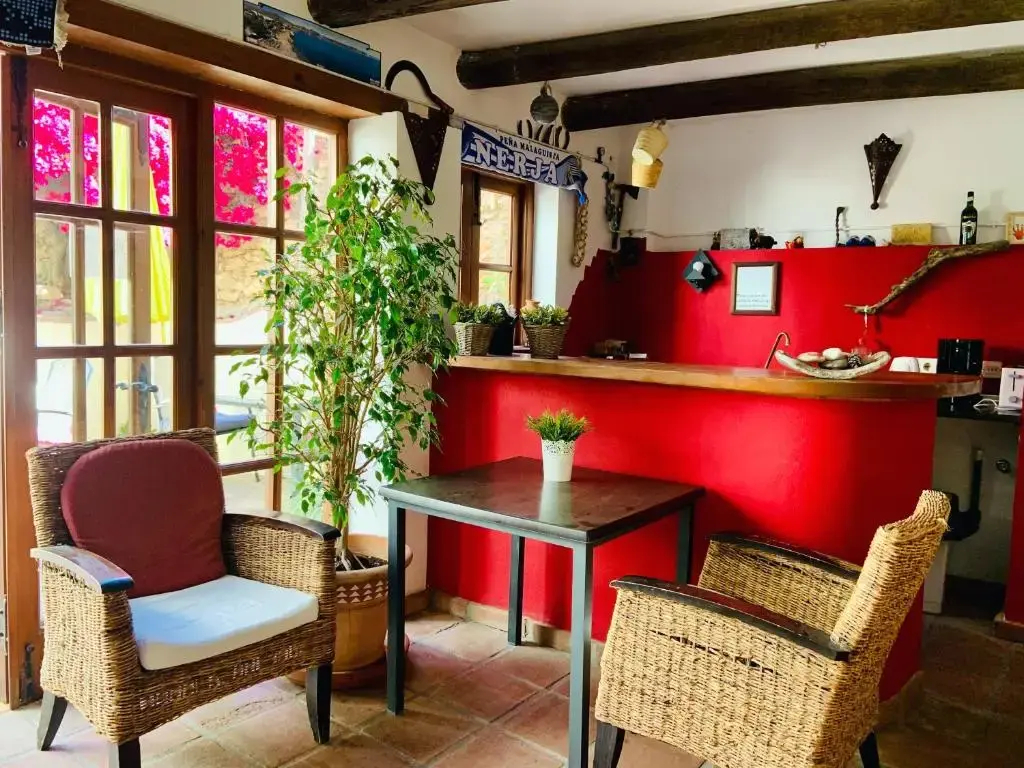 Rincón con barra roja, mesa y sillones de mimbre junto a una ventana con buganvillas