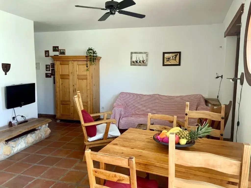Salón con sofá, armario de madera, televisor y mesa de comedor con frutero