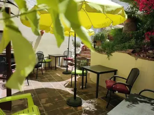 Patio con sombrillas amarillas, mesas y sillas de forja entre plantas