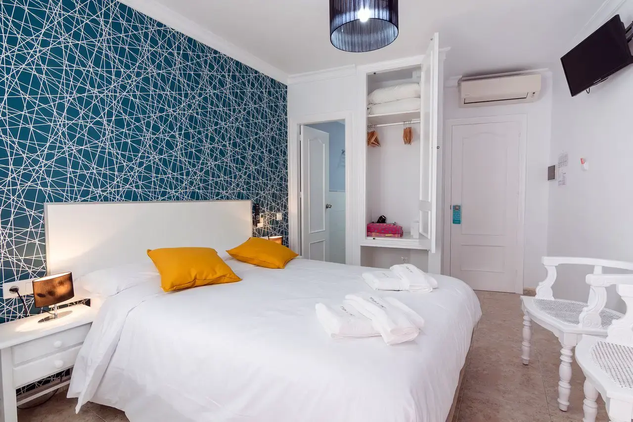 Dormitorio con cama de matrimonio, pared de papel geométrico azul y armario abierto
