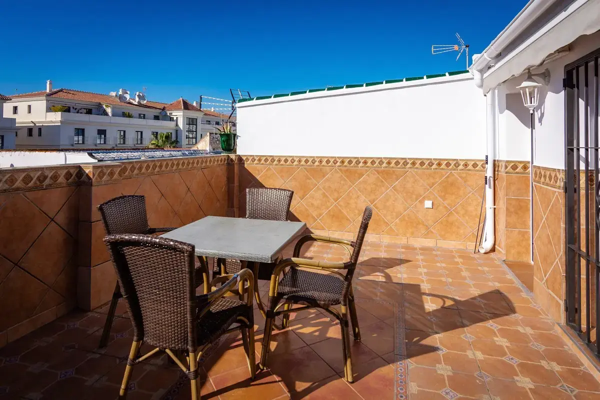 Terraza con mesa y sillas de ratán, paredes de azulejo y cielo despejado
