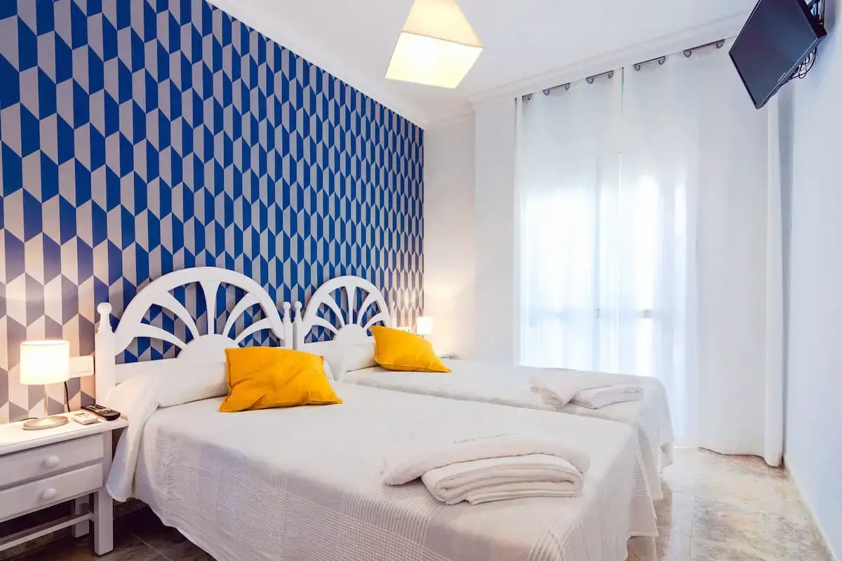 Habitación con dos camas de cabecero blanco y pared de rombos azules