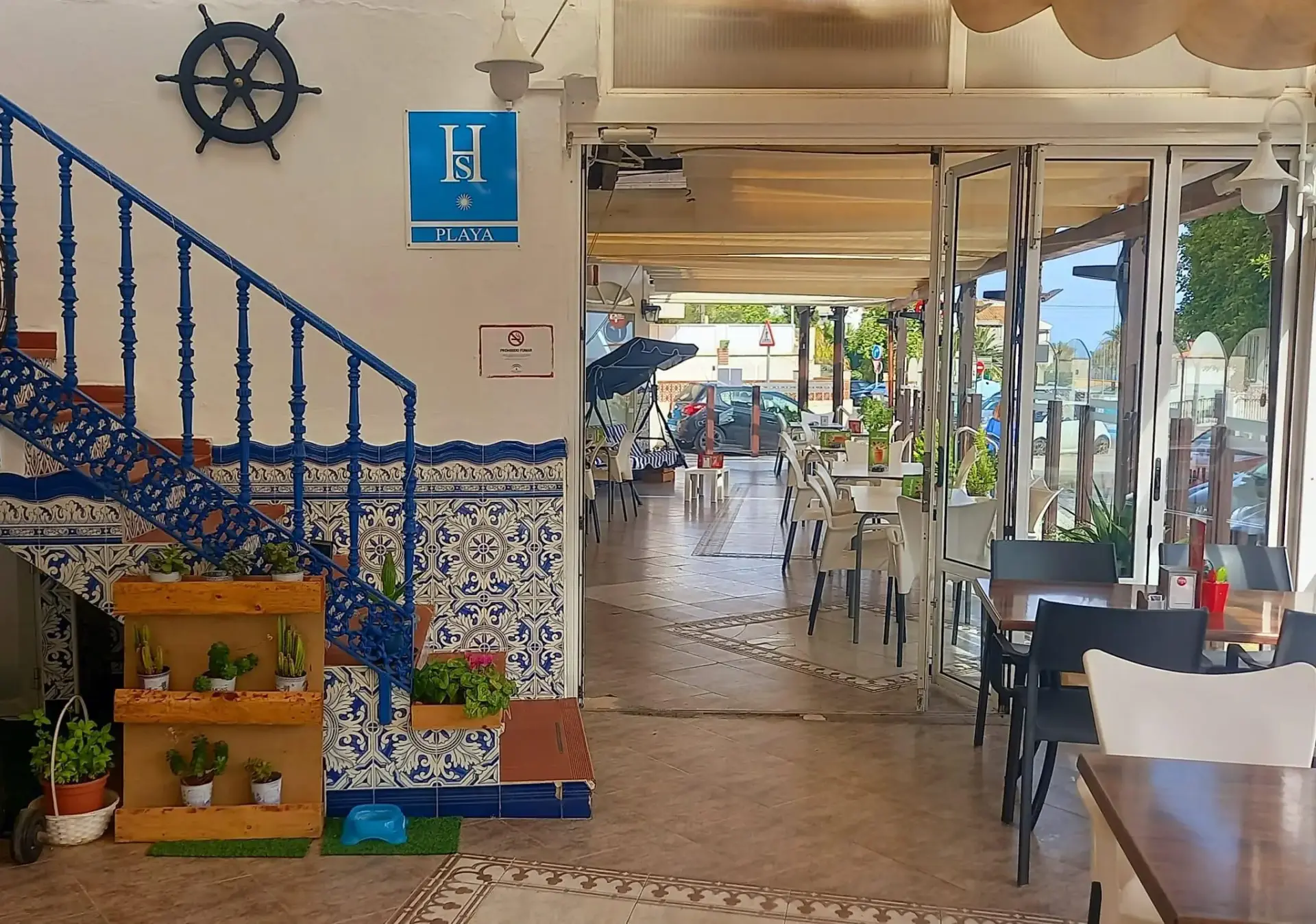 Escalera de azulejos azules y blancos, placa de hostal playa y mesas de la cafetería
